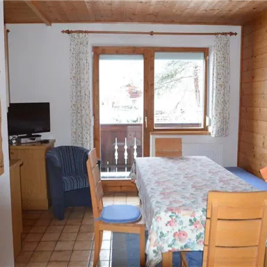 A cozy living area with a dining table, wood paneling, and a large window. The decor is simple and inviting, with blue and orange accent colors.
