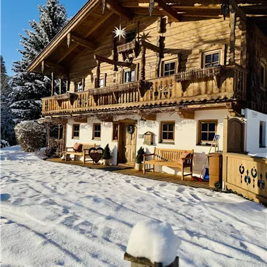 A traditional wooden house in the snow with a cozy balcony. The surroundings are wintry and peaceful.