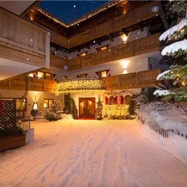 Ein gemütlicher Innenhof eines Hotels, bedeckt mit frischem Schnee. Lichter und festliche Dekoration schaffen eine einladende Atmosphäre.