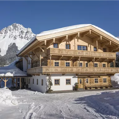 A cozy wooden house in the snow with a beautiful mountain in the background. The sunny winter landscape radiates peace and idyllic charm.
