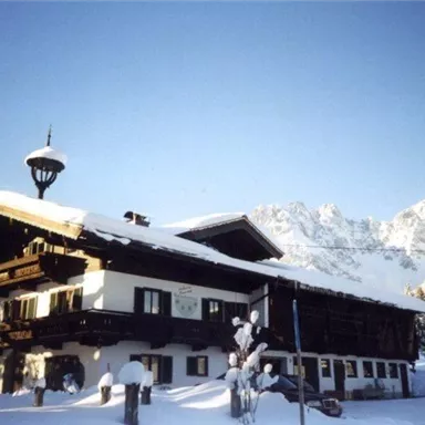 Ein charmantes Berghaus im Winter, bedeckt mit Schnee. Im Hintergrund sind beeindruckende Berge zu sehen.