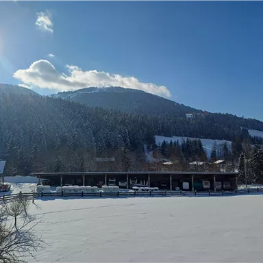 A snowy landscape with mountains in the background and a building on the edge of a frozen lake. The sky is clear and sunny.