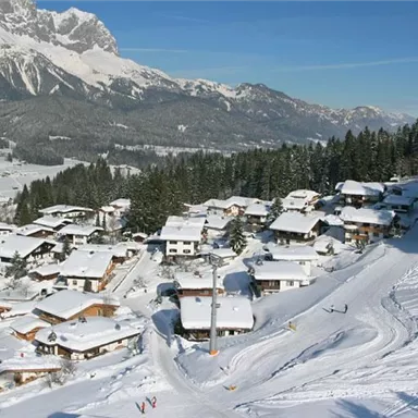 Ein verschneites Dorf in den Alpen mit bunten Häusern. Im Hintergrund sind beeindruckende Berge sichtbar.