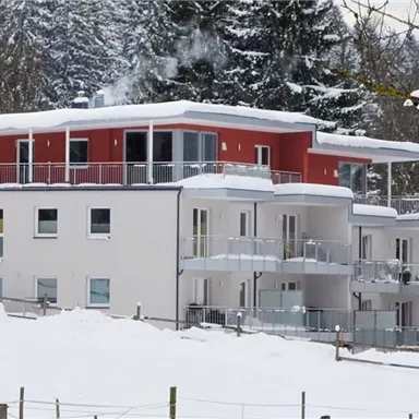 A modern building in the snow with red and white elements. Snow-covered trees are visible all around.
