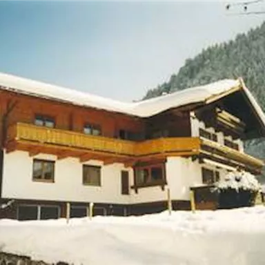 Ein schönes Holzhaus in den Bergen, umgeben von schneebedeckten Tannen. Der Himmel ist klar und die Landschaft wirkt friedlich.