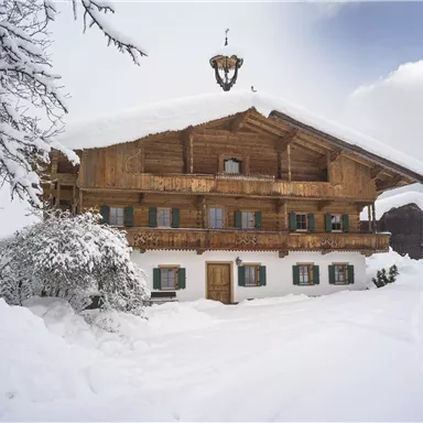 Ein traditionelles Holzhaus im Schnee mit einem schönen, schneebedeckten Außenbereich. Die Umgebung ist winterlich und ruhig.