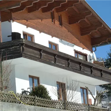 A traditional house in alpine style with wood embellishments. The clear sky and the adjacent trees create a tranquil atmosphere.