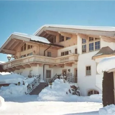 An elegant chalet in the snow with a spacious balcony. The entrance is surrounded by a picturesque snowy landscape.