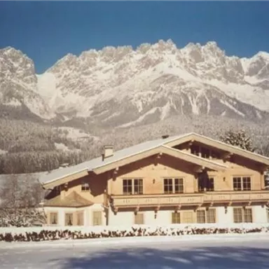 A charming wooden house in a snowy winter landscape. Majestic mountains rise in the background under a clear sky.