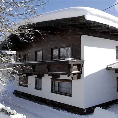 A cozy house in the snow with a classic wooden roof. The surroundings are covered in fresh, white snow.