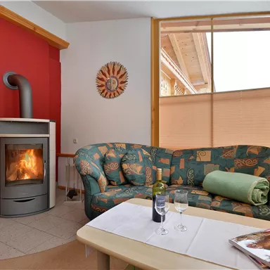 Ein gemütlicher Wohnraum mit einem grünen Sofa und einem modernen Kamin. Der Raum hat helle Fenster und eine warme Atmosphäre.