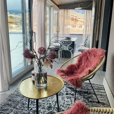 A stylish veranda with modern furniture. A round table with a vase and comfortable chairs offers an inviting view outside.