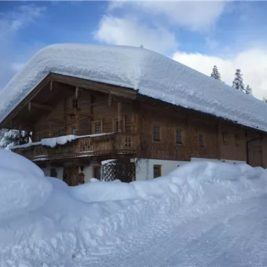 A cozy wooden house with a snow-covered roof. The surroundings are wintry and covered with a lot of snow.