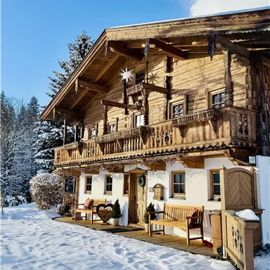 A cozy wooden house in winter, surrounded by snow and fir trees. The balconies are decorated with Christmas ornaments.
