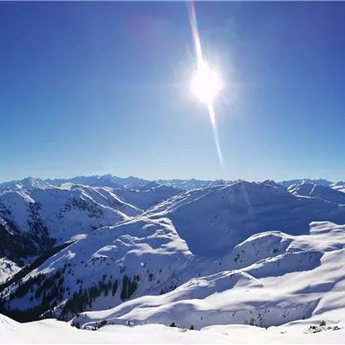 Eine weite, schneebedeckte Berglandschaft unter einem strahlend blauen Himmel. Die Sonne scheint hell über den majestätischen Gipfeln.