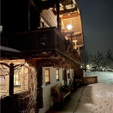 A cozy wooden house at night, illuminated by warm light. Surrounded by snow and a winter landscape.