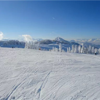 Ein verschneites Berglandschaft mit strahlend blauem Himmel. Skifahrer sind in der Ferne zu sehen.