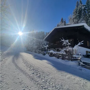 Ein großes, gemütliches Haus in einer verschneiten Landschaft. Die Sonne strahlt am klaren blauen Himmel.