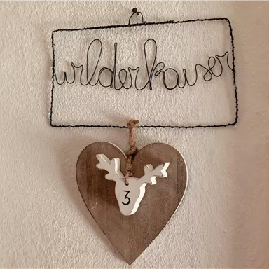 Ein dekoratives Schild mit der Aufschrift "Wilderkaiser" hängt an der Wand. Darunter befindet sich ein herzförmiges Holzschild mit einem weißen Hirschkopf.