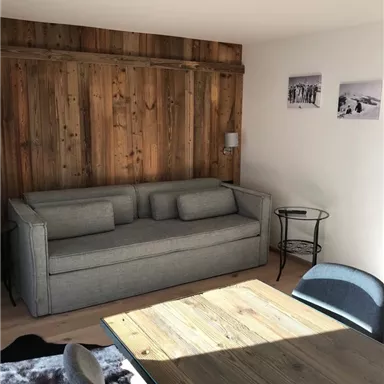 A cozy living space with a gray sofa and a wooden table. The wooden panels on the wall and the pictures give the room a warm atmosphere.