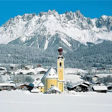 A picturesque village in the snow with a beautiful yellow church. In the background, an impressive mountain landscape rises.