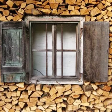 A window with open shutters, surrounded by stacked wood. The wood is neatly arranged and gives the image a rustic charm.