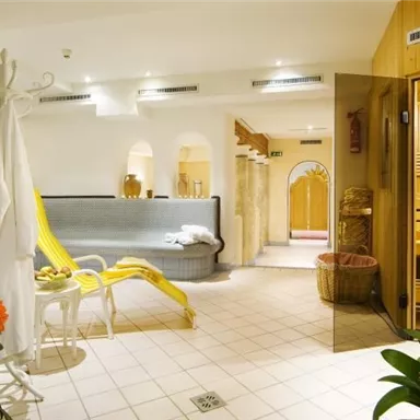 Ein entspannender Wellnessbereich mit einer Sauna und gemütlichen Sitzecken. Die Einrichtung ist hell und freundlich, umgeben von Pflanzen und Orangetönen.