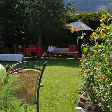 Ein schöner Garten mit bunten Blumen und bequemen Liegen. Im Hintergrund steht ein Sonnenschirm und es herrscht eine entspannte Atmosphäre.