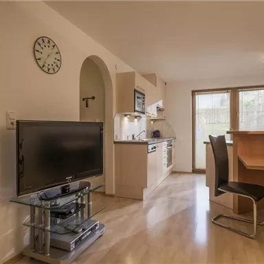 Eine moderne Küche mit angrenzendem Wohnbereich. Der Raum ist hell und mit einem TV, Esstisch und Stühlen ausgestattet.