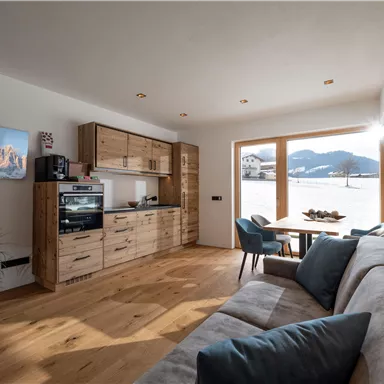 Ein modernes Wohnzimmer mit Holzregalen und einer gemütlichen Couch. Große Fenster bieten einen Blick auf die umliegenden Berge.