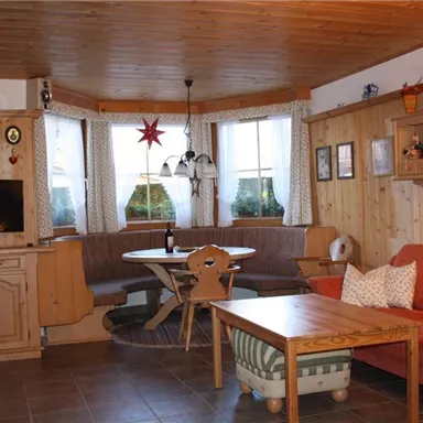 Ein gemütliches Wohnzimmer mit Holzpaneelen und warmen Farben. Es gibt eine Sitzgelegenheit, einen Esstisch und einen Fernseher.