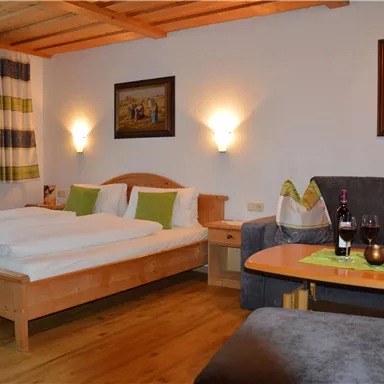 Ein gemütliches Schlafzimmer mit einem Doppelbett und einem Sofa. Die Wände sind mit Gemälden dekoriert, und es gibt sanfte Beleuchtung.