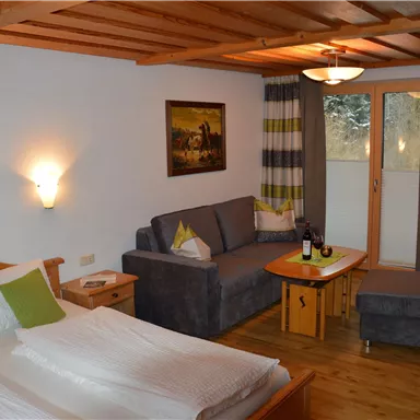 Ein komfortables Hotelzimmer mit einem Doppelbett und einer Sofa-Ecke. Die Einrichtung ist gemütlich und hell, mit einem Balkon und Kunstwerken an den Wänden.