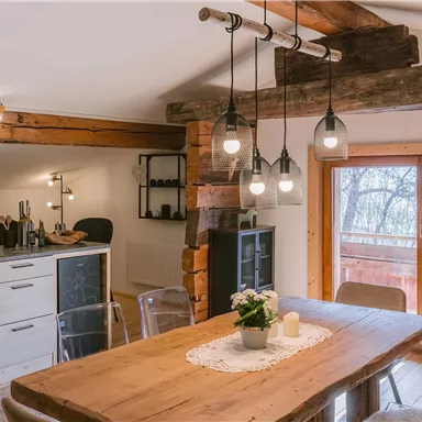 Eine moderne Küche mit einem großen Holztisch und eleganten Stühlen. Die warmen Holzdetails und die hängenden Lampen schaffen eine gemütliche Atmosphäre.