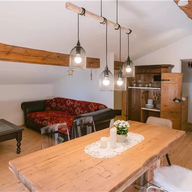 Ein gemütlicher Wohnraum mit Holzbalken und einem roten Sofa. Der Tisch ist aus Holz gedeckt und wirkt einladend.