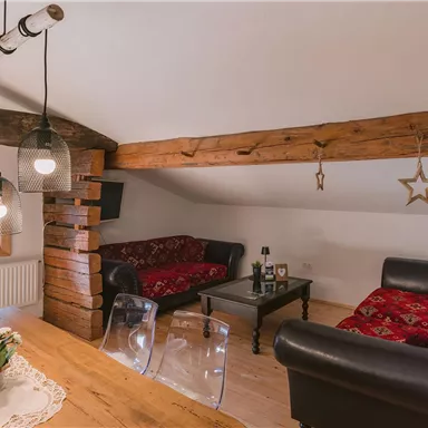 Eine gemütliche Wohnstube mit Holzbalken und Platz für Entspannung. Zwei komfortable Sofas und ein Essbereich schaffen eine einladende Atmosphäre.