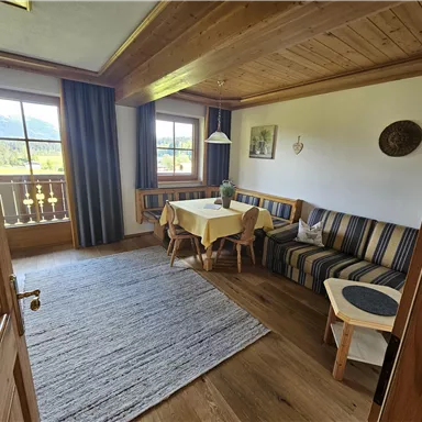 Ein gemütlicher Wohnraum mit Holzvertäfelungen und einem großen Fenster. Ein Esstisch und eine Sitzgelegenheit laden zum Verweilen ein.