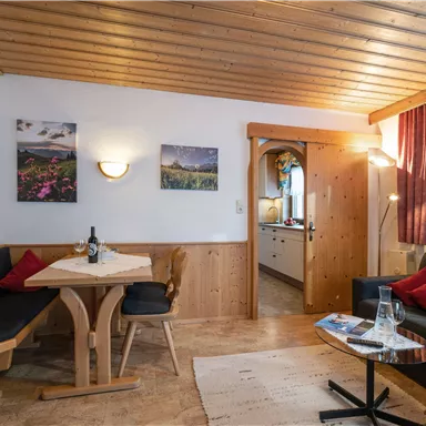 Ein gemütlicher Wohnraum mit Holzdecke und einem Tisch. Die Einrichtung ist rustikal, mit einem Sofa und bunten Kissen.