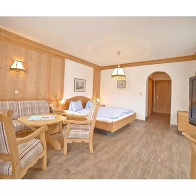 Ein gemütliches Zimmer mit Holzdetails, einer Sitzecke und einem Doppelbett. Es gibt einen Fernseher und warmes Licht für eine einladende Atmosphäre.