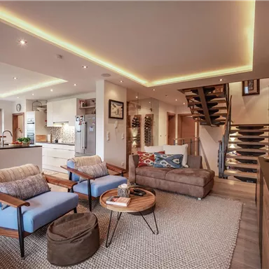 Ein modernes Wohnzimmer mit bequemen blauen Sesseln und einem stilvollen Couchtisch. Die helle, offene Küche ist gut ausgestattet und der Raum hat große Fenster mit schönem Ausblick.