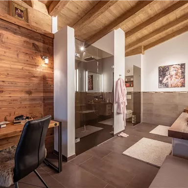 Ein modernes Badezimmer mit Holzvertäfelung und einem eleganten Duschbereich. Ein Schminktisch und ein gemütlicher Sitzbereich runden das einladende Ambiente ab.