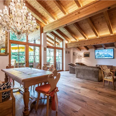 An inviting living room with a wooden ceiling and large windows that let in plenty of light. The space includes a dining table, comfortable seating, and a television.