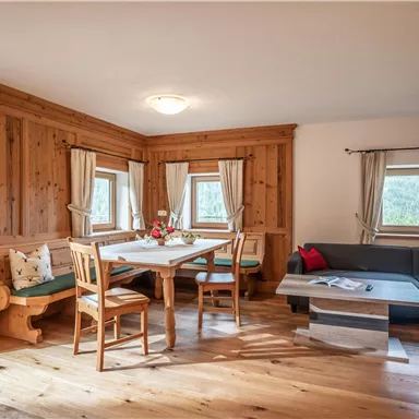 A cozy kitchen-living room with wooden furniture and a large dining table. The windows let in a lot of light, and the decor is warm and inviting.