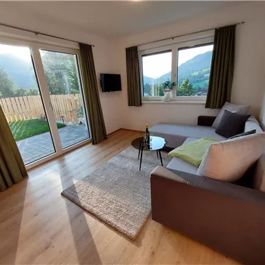 Ein gemütlicher Wohnraum mit einem Sofa und einem kleinen Tisch. Große Fenster bieten Ausblick auf die Natur.