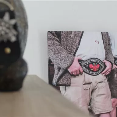 A photograph of three people in traditional clothing, each wearing a belt with a large buckle. In the foreground, a decorative piece is visible.