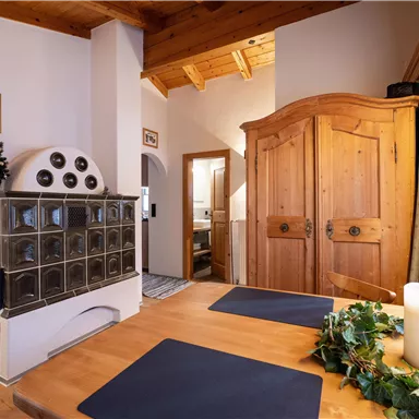 Ein einladender Wohnraum mit einem Holzofen und einem großen Holzschrank. Der Tisch ist gedeckt und es gibt eine dekorative Kerze.