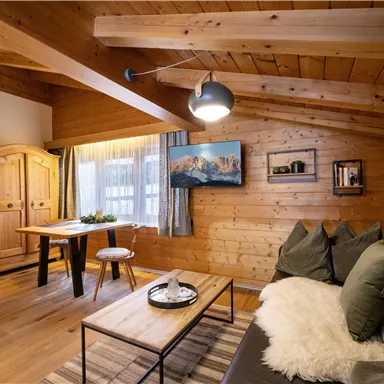 Ein gemütlicher Raum mit Holzverkleidung, einem modernen Sofa und einem Tisch. Großzügige Fenster sorgen für viel Licht und eine einladende Atmosphäre.