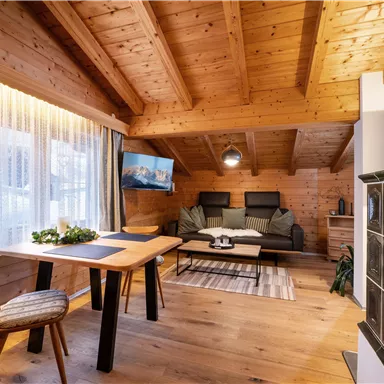 Gemütliches Wohnzimmer mit Holzdecken und -wänden. Ein Esstisch und eine Couch schaffen eine einladende Atmosphäre.