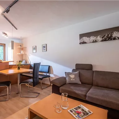 Ein modernes Wohnzimmer mit einem komfortablen Sofa und einem Esstisch. Große Fenster sorgen für helles Licht und eine angenehme Atmosphäre.