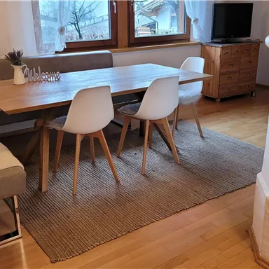 Ein gemütlicher Essbereich mit einem Holzstutztisch und modernen Stühlen. Die Umgebung ist hell und freundlich mit großen Fenstern.